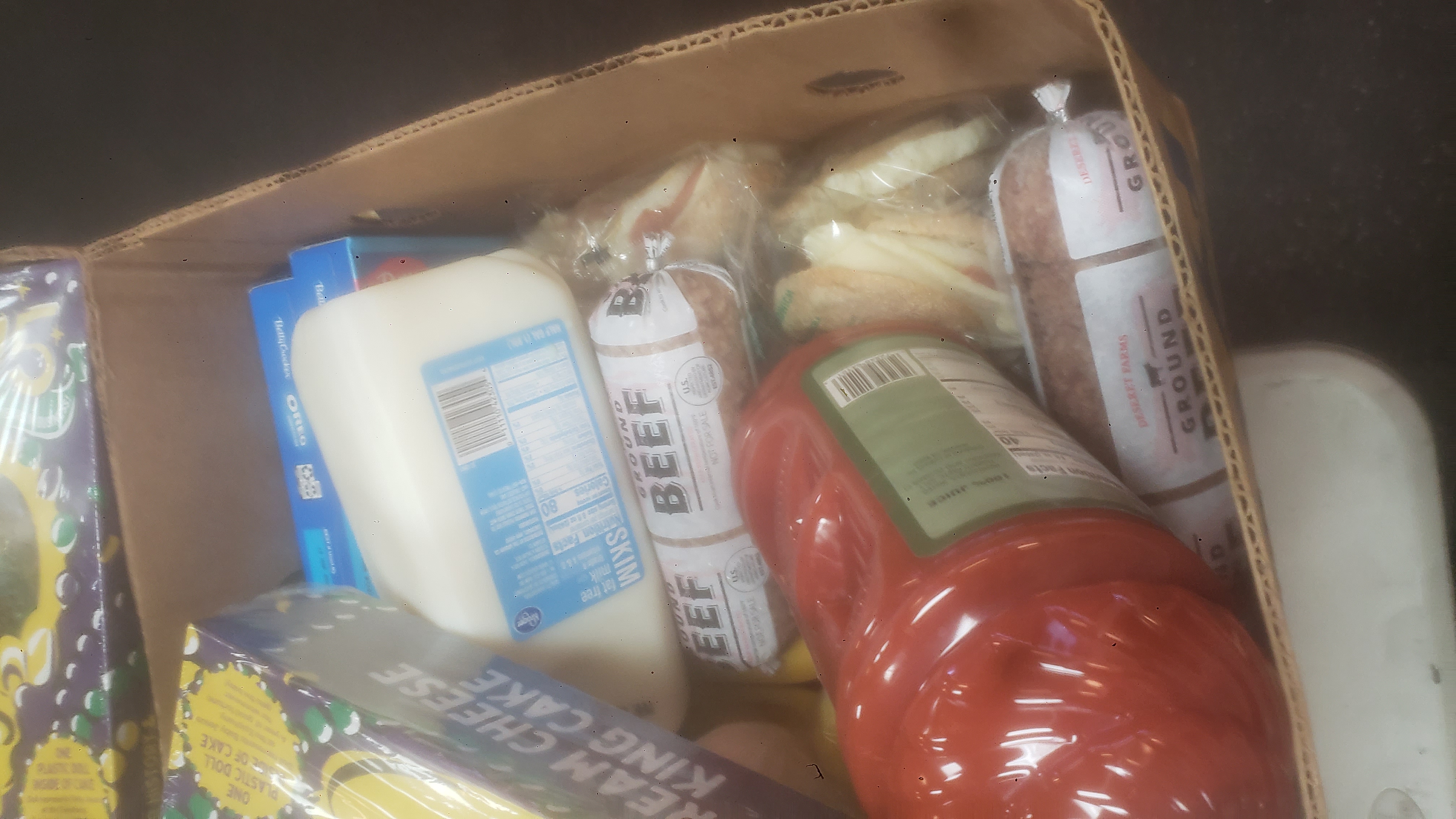 Banana box full of food such as a sheet of king cake and gallon of milk.